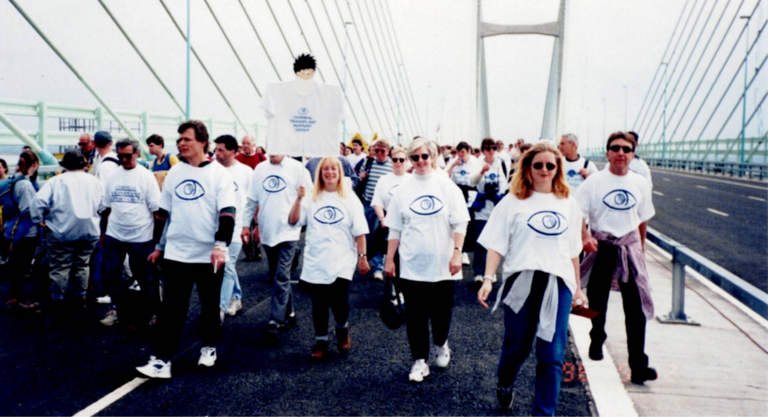 Group of people walking along a bridge holding signs