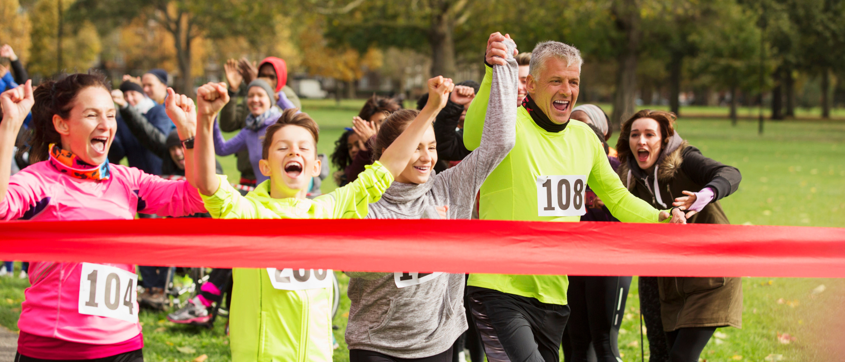 a group of people holding hands running towards a red finish line ribbon