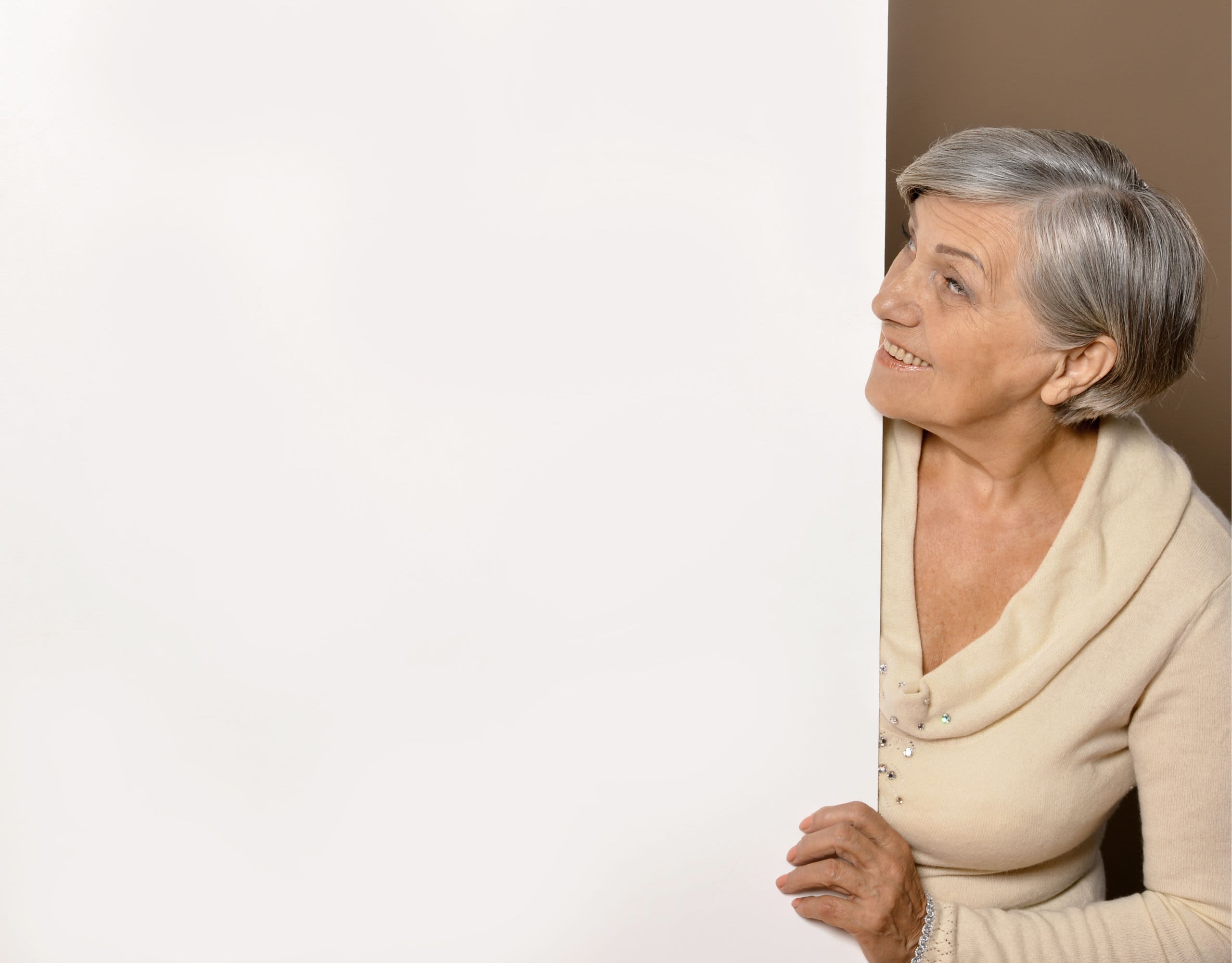 Elderly woman peering from behind a large screen and smiling up at the text on the screen