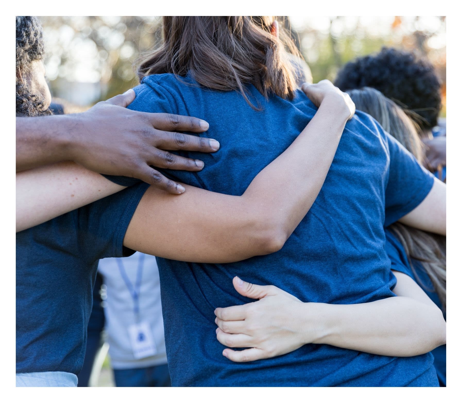 Group of people wearing blue t-shirts huddled in circle arm in arm