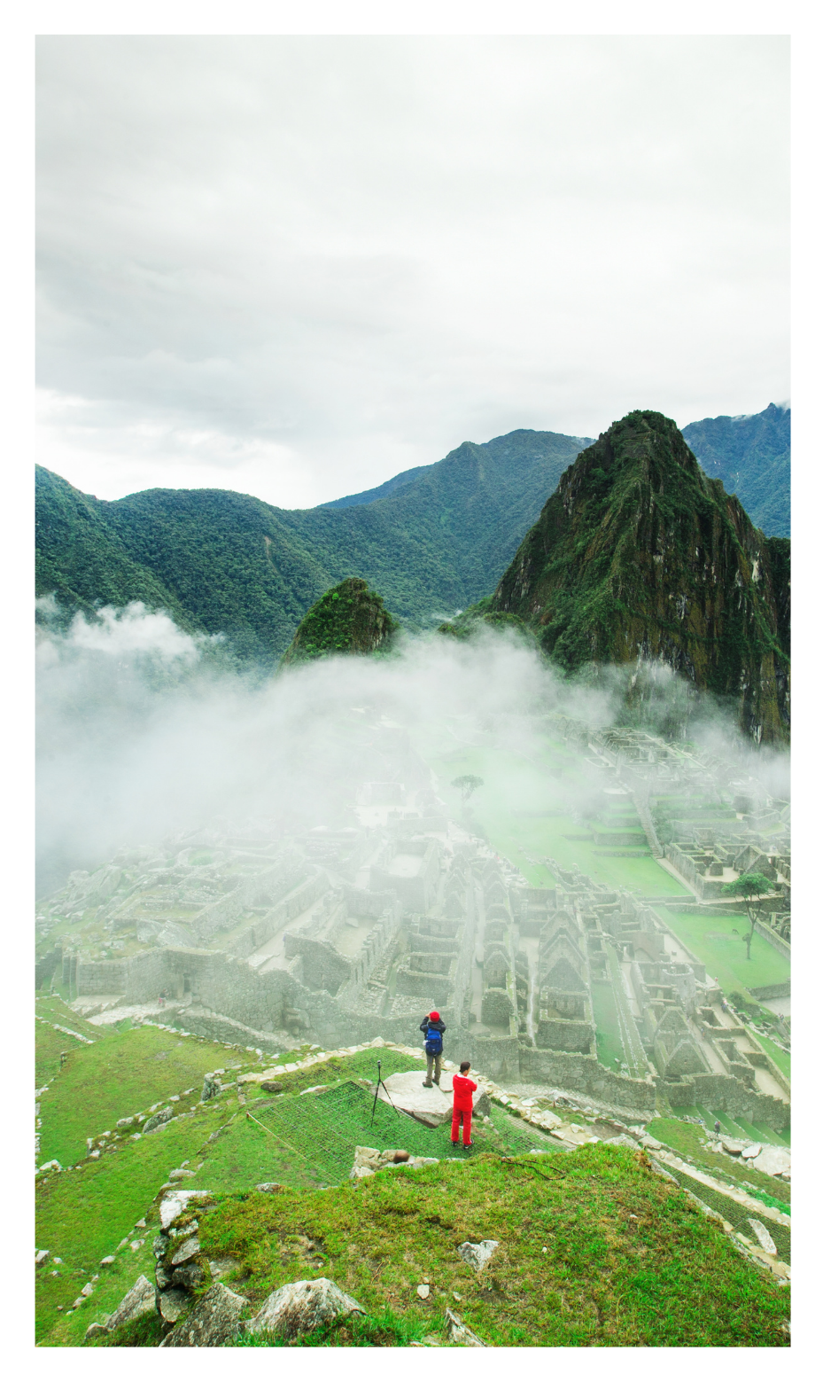 Summit of Machu Picchu shroud in clouds, two people looking down to the ruins from the summit